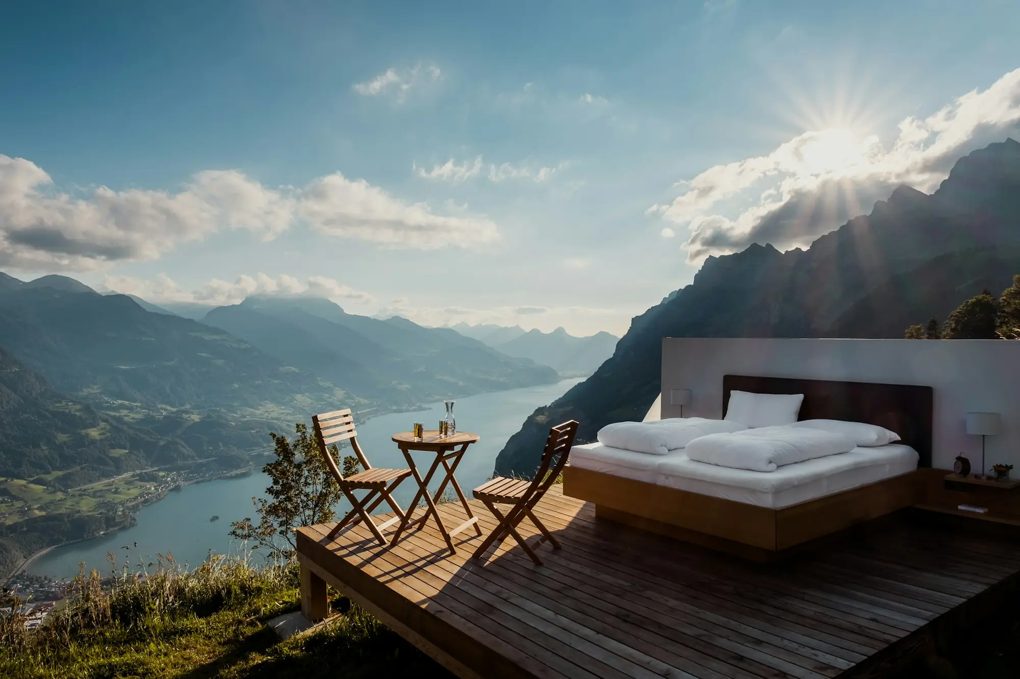 Holzterrasse mit Bett und Blick über einen Bergsee bei Sonnenaufgang